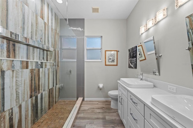 bathroom with a tile shower, wood-type flooring, toilet, and vanity