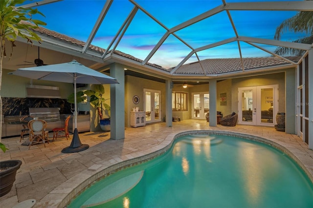 pool at dusk featuring glass enclosure, a patio, french doors, and exterior kitchen