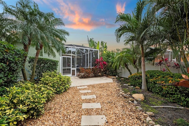 yard at dusk featuring a patio and glass enclosure