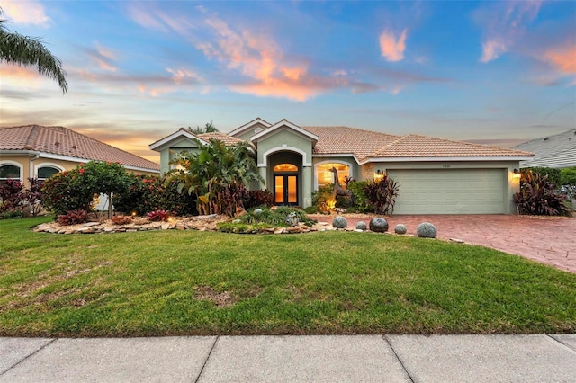 mediterranean / spanish home with a garage, a lawn, and french doors