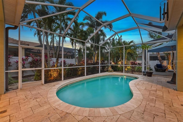 pool at dusk with glass enclosure and a patio area