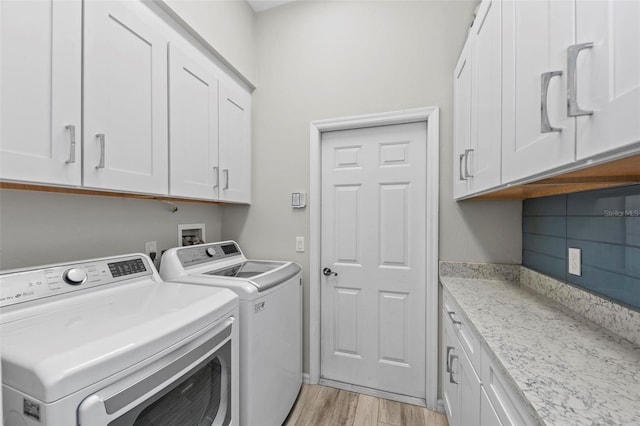 laundry room with washing machine and dryer, light hardwood / wood-style flooring, and cabinets