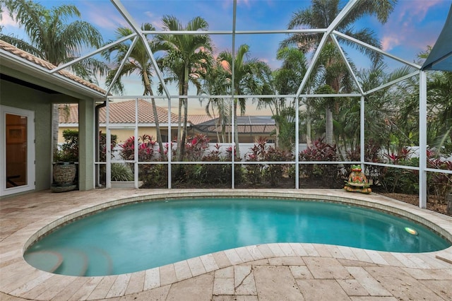 pool at dusk featuring glass enclosure and a patio area