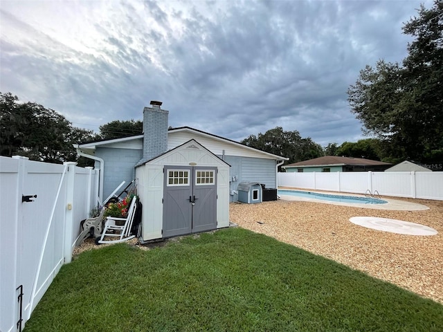 rear view of property featuring a storage shed, a fenced in pool, and a lawn