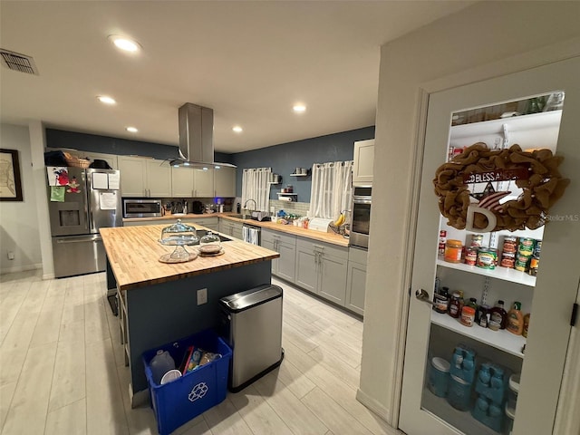 kitchen featuring appliances with stainless steel finishes, wood counters, island exhaust hood, a center island, and light hardwood / wood-style floors