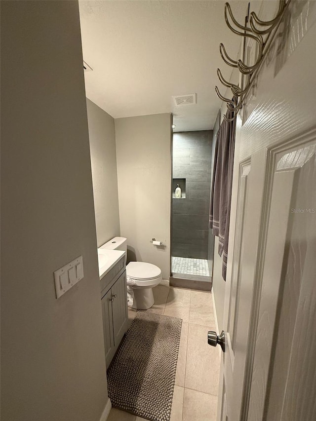 bathroom featuring vanity, tile patterned floors, toilet, and tiled shower