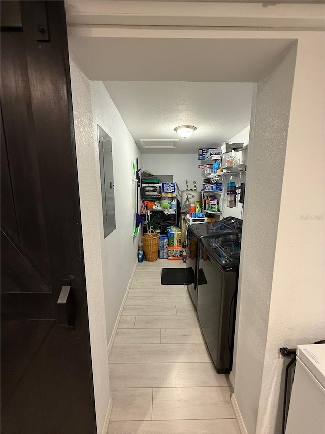 clothes washing area featuring light hardwood / wood-style flooring, washer and clothes dryer, electric panel, and a textured ceiling