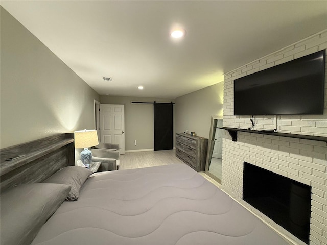 bedroom with a brick fireplace, light hardwood / wood-style floors, and a barn door