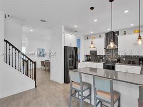 kitchen featuring hanging light fixtures, white cabinets, black fridge, a breakfast bar, and backsplash