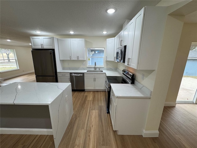 kitchen featuring sink, white cabinetry, light stone counters, stainless steel appliances, and light hardwood / wood-style floors