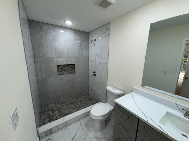 bathroom with vanity, a textured ceiling, toilet, and tiled shower