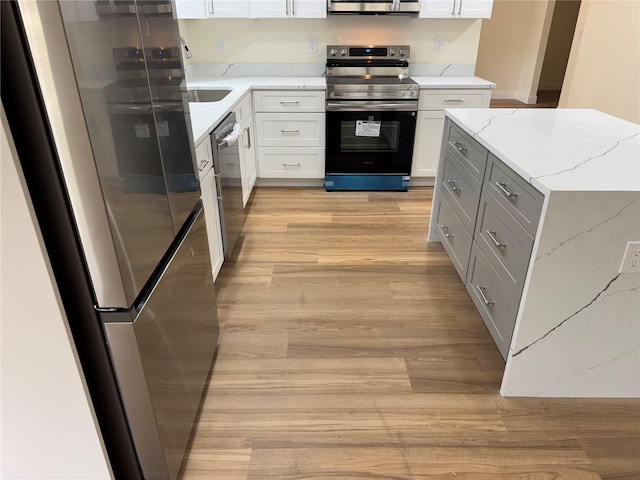 kitchen featuring white cabinetry, appliances with stainless steel finishes, light stone countertops, and light wood-type flooring