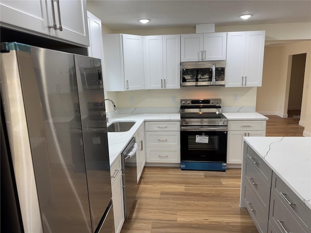 kitchen featuring sink, white cabinets, stainless steel appliances, light stone countertops, and light hardwood / wood-style flooring