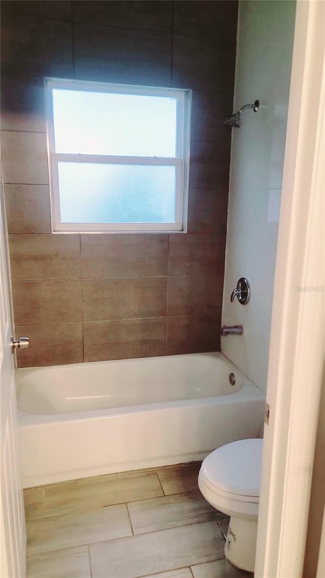 bathroom featuring tiled shower / bath combo, toilet, and a wealth of natural light