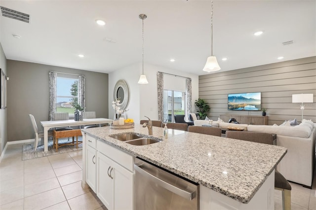 kitchen featuring pendant lighting, white cabinets, sink, wood walls, and stainless steel dishwasher