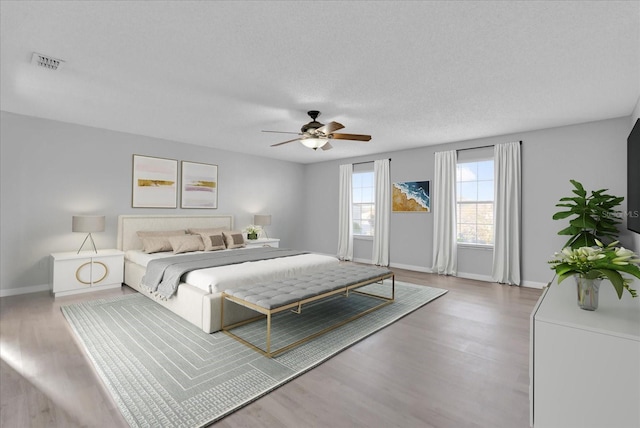 bedroom with visible vents, baseboards, a textured ceiling, and wood finished floors