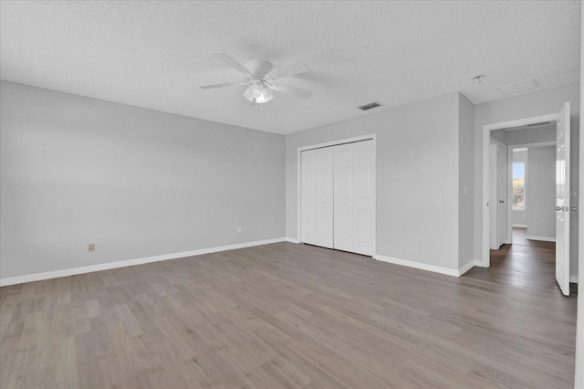 unfurnished bedroom with visible vents, a textured ceiling, wood finished floors, a closet, and baseboards