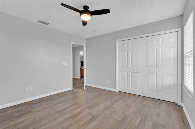 unfurnished bedroom featuring wood finished floors, baseboards, visible vents, a closet, and a textured ceiling