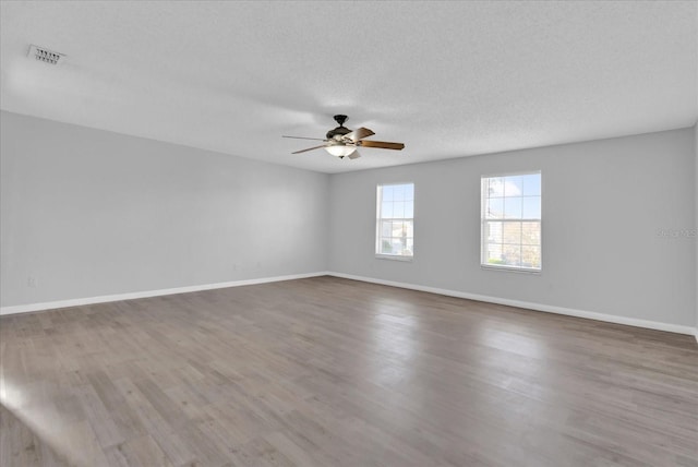 unfurnished room with baseboards, wood finished floors, visible vents, and a textured ceiling