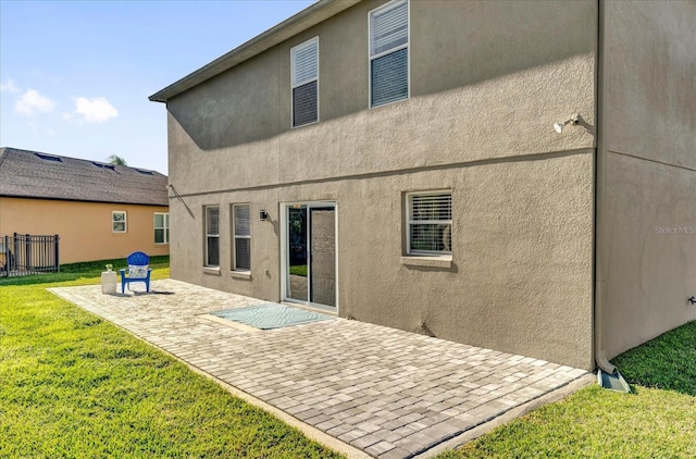 back of property with a patio area, stucco siding, a yard, and fence