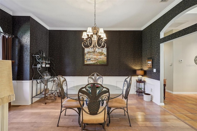 dining space with hardwood / wood-style floors, ornamental molding, and an inviting chandelier