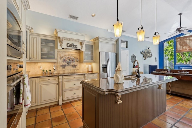 kitchen with hanging light fixtures, cream cabinets, a kitchen island with sink, decorative backsplash, and stainless steel appliances