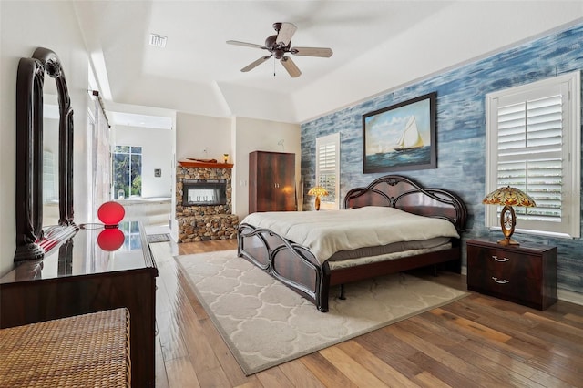 bedroom featuring a stone fireplace, hardwood / wood-style floors, and ceiling fan