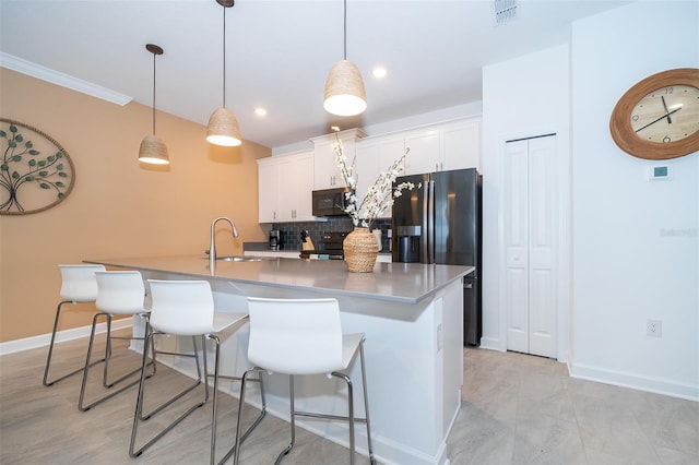 kitchen with a large island with sink, white cabinets, sink, hanging light fixtures, and black fridge