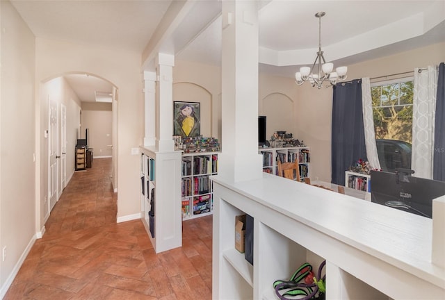 corridor with light parquet floors, a raised ceiling, and a notable chandelier