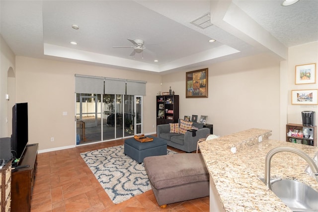 living room with ceiling fan, a raised ceiling, sink, and a textured ceiling