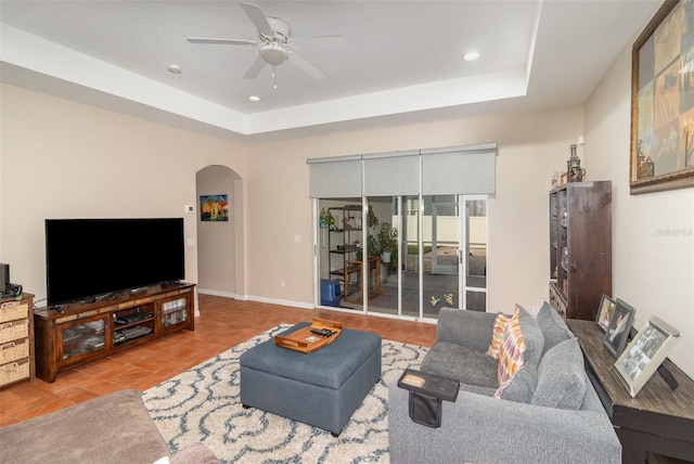 tiled living room with a tray ceiling and ceiling fan