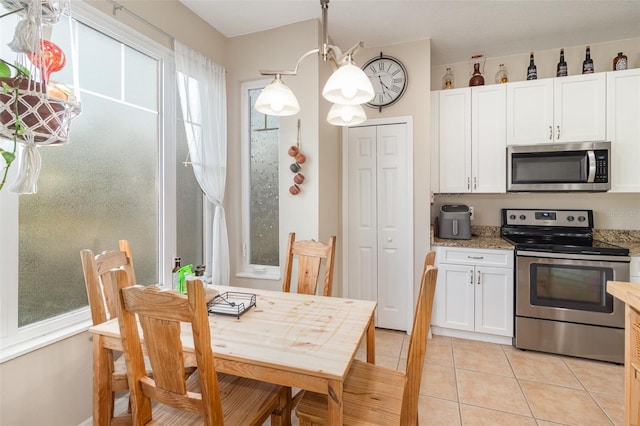 kitchen with stainless steel appliances, light tile patterned floors, hanging light fixtures, and white cabinets