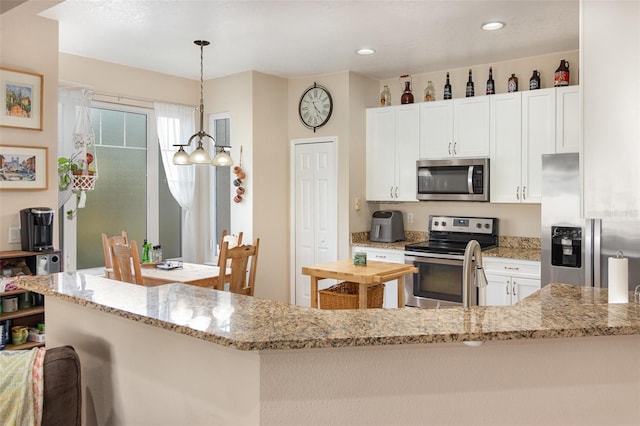 kitchen featuring light stone countertops, appliances with stainless steel finishes, pendant lighting, and white cabinets