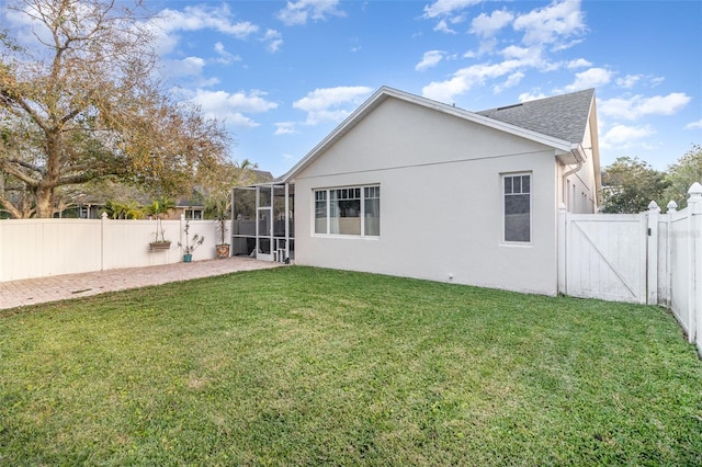 rear view of property with glass enclosure, a patio, and a lawn