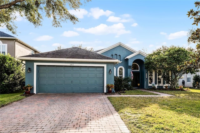 ranch-style home featuring a garage, a front yard, decorative driveway, and stucco siding