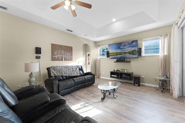 living room with light wood finished floors, visible vents, arched walkways, and a raised ceiling