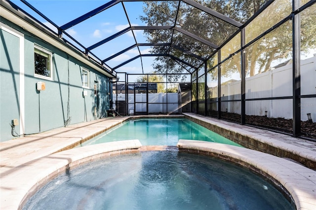 view of swimming pool with glass enclosure, a pool with connected hot tub, and fence