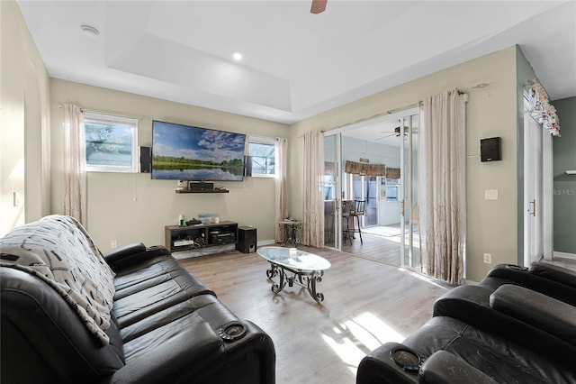 living room featuring light wood-style floors, a tray ceiling, ceiling fan, and baseboards