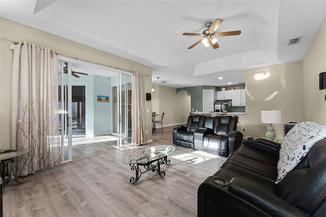 living room featuring a ceiling fan, a raised ceiling, visible vents, and light wood-style floors