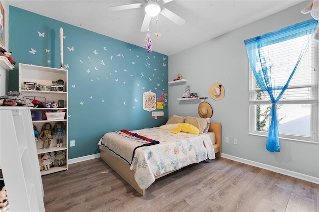 bedroom featuring an accent wall, multiple windows, wood finished floors, and baseboards