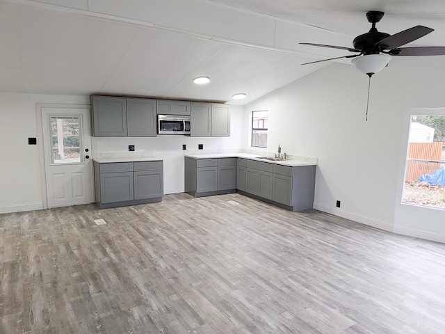 kitchen featuring gray cabinetry, sink, vaulted ceiling, and light wood-type flooring