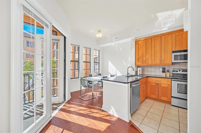 kitchen with sink, light tile patterned floors, kitchen peninsula, stainless steel appliances, and backsplash