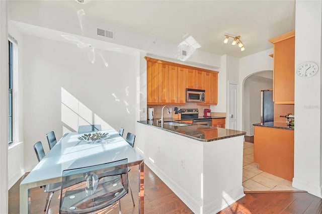 kitchen with sink, dark stone countertops, stainless steel appliances, tasteful backsplash, and kitchen peninsula