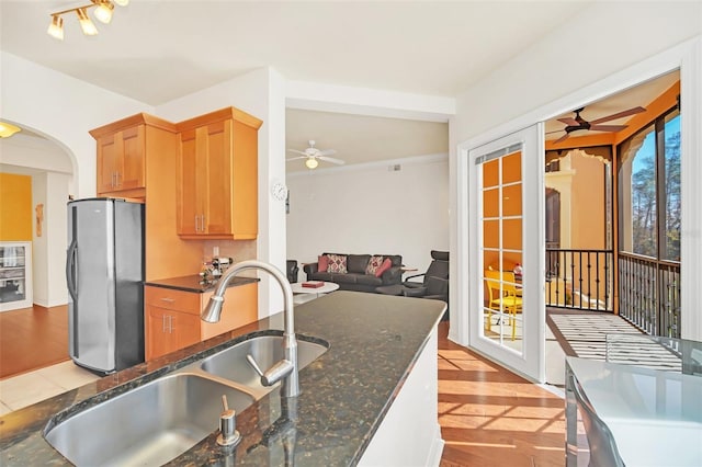 kitchen featuring ceiling fan, dark stone counters, stainless steel fridge, and sink