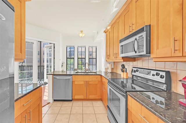 kitchen featuring stainless steel appliances, sink, dark stone countertops, and light tile patterned floors