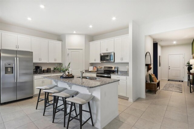 kitchen with white cabinets, stainless steel appliances, light stone counters, and a center island with sink