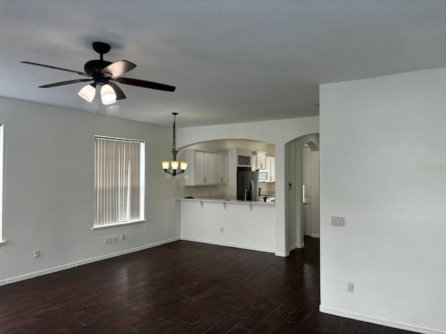 unfurnished living room with ceiling fan with notable chandelier and dark hardwood / wood-style flooring