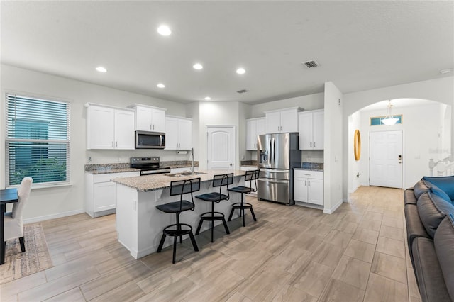 kitchen featuring a kitchen bar, appliances with stainless steel finishes, white cabinetry, sink, and a center island with sink