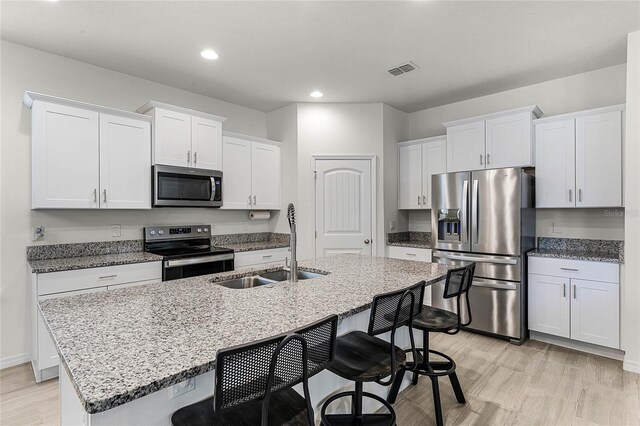 kitchen featuring light stone countertops, white cabinetry, stainless steel appliances, an island with sink, and a breakfast bar area