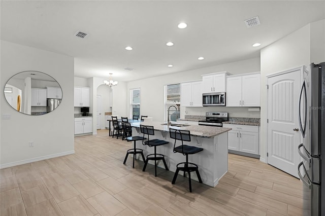 kitchen with appliances with stainless steel finishes, sink, white cabinetry, a center island with sink, and a breakfast bar area